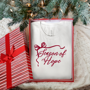 White t-shirt with 'Season of Hope' text under a Christmas tree with a gift box.