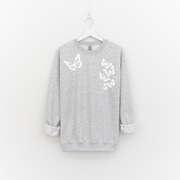Woman wearing an ash grey crewneck with six white butterflies symbolizing the 1 in 6 infertility statistic.