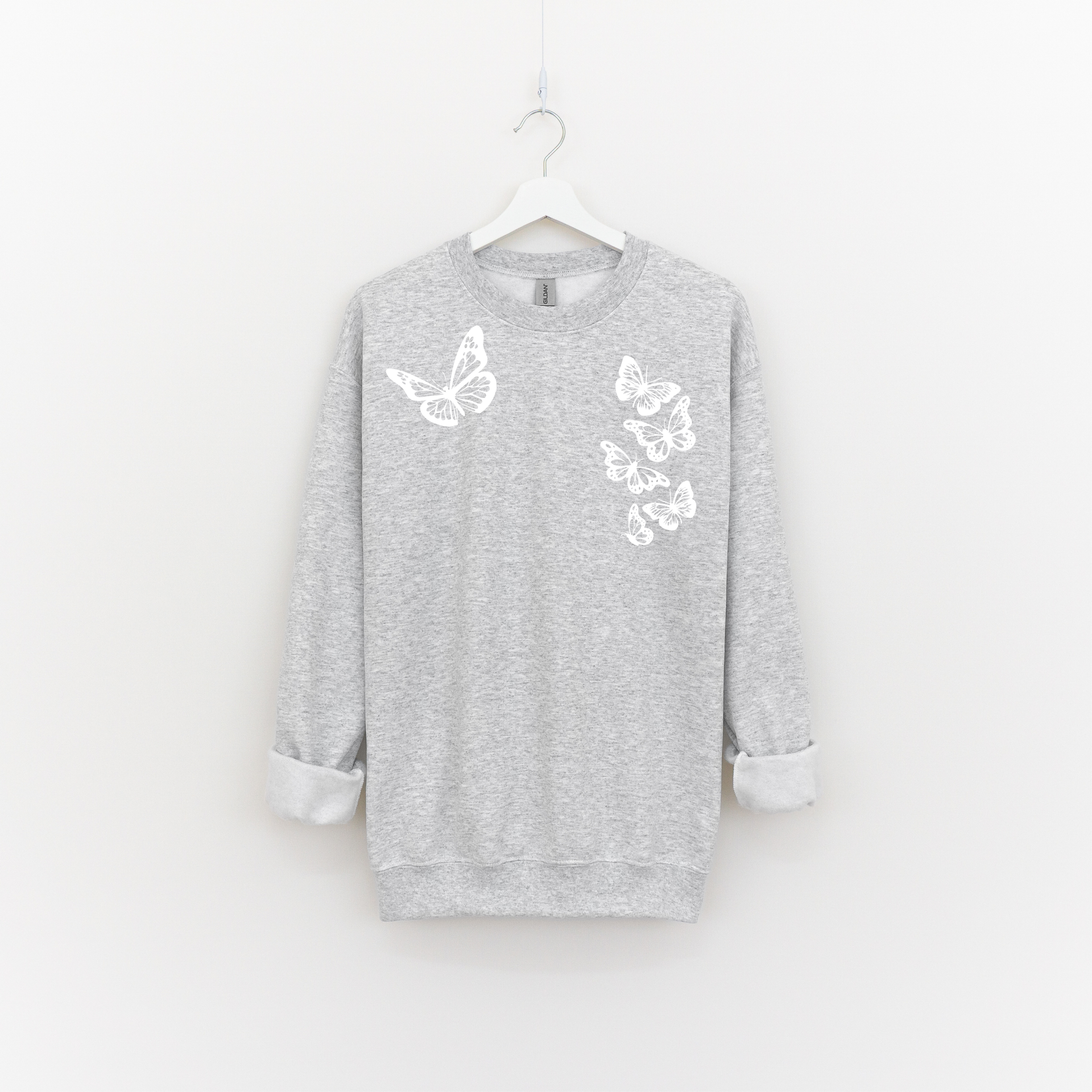 Woman wearing an ash grey crewneck with six white butterflies symbolizing the 1 in 6 infertility statistic.