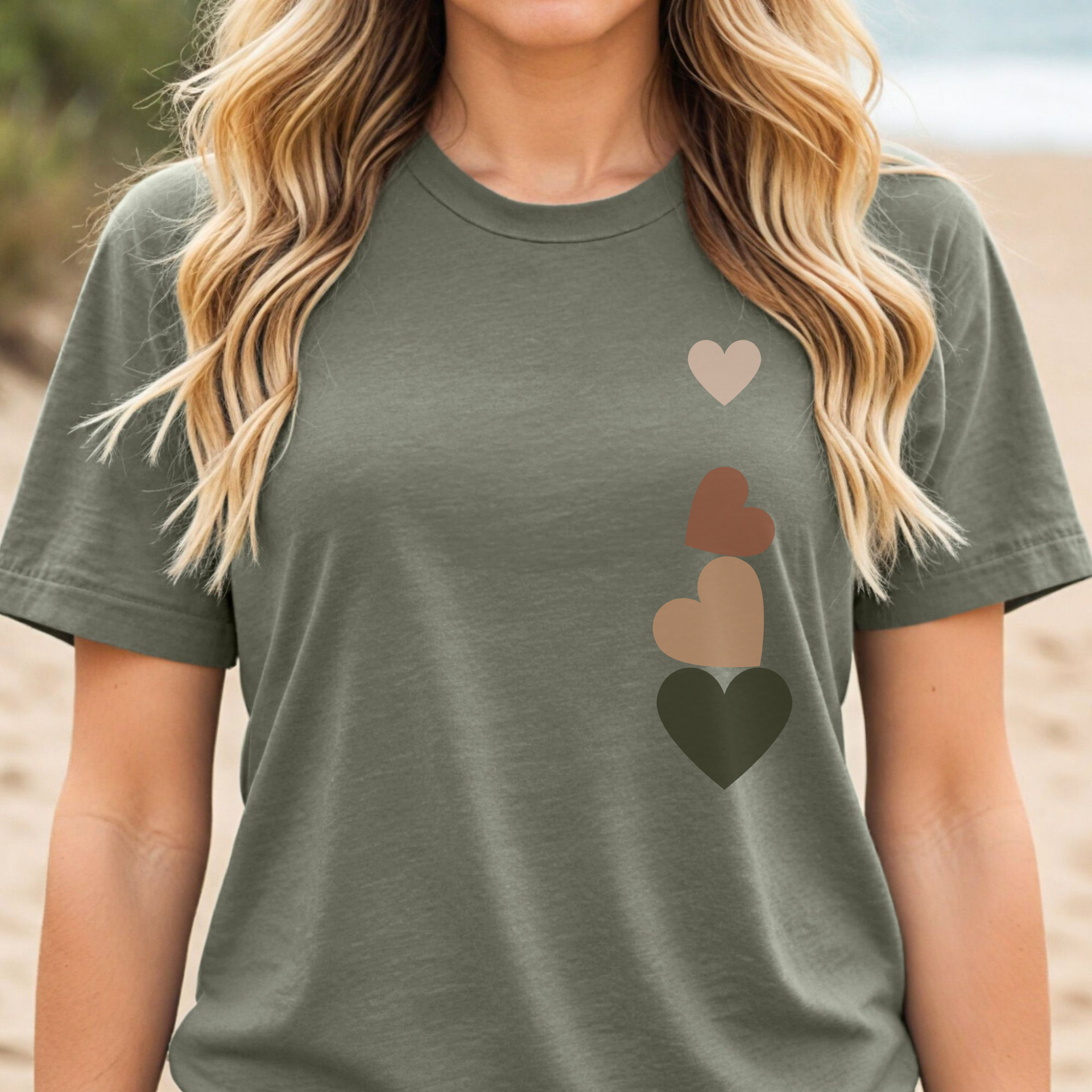 Woman wearing an olive green t-shirt with cascading earth-tone hearts design, subtly honoring the 1 in 4 women who experience miscarriage; minimalist fertility and pregnancy loss awareness tee.