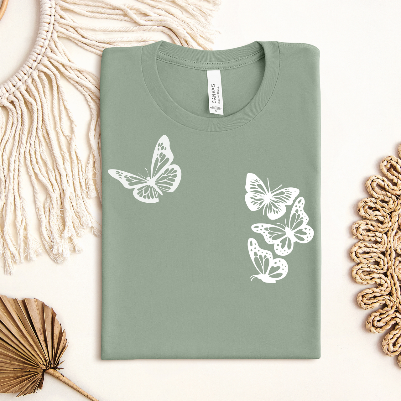 Sage green t-shirt with white butterfly designs on a light background white butterflies symbolizing the 1 in 4 miscarriage statistic.