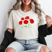 Woman wearing a cream-colored t-shirt with six red poppy flowers symbolizing the 1 in 6 infertility community, sitting casually indoors.