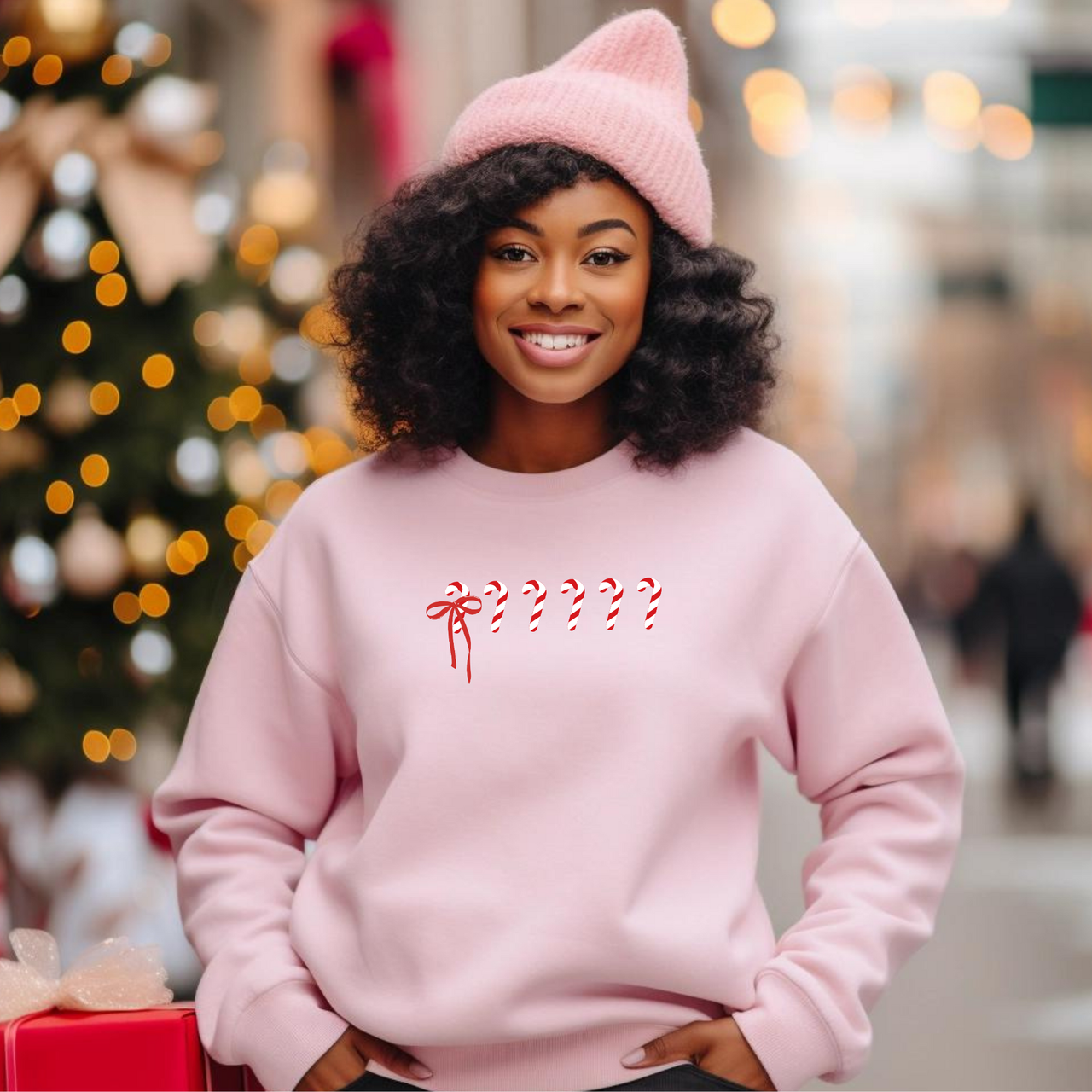 Woman wearing a pink holiday crewneck with a subtle 1 in 6 candy cane design honoring infertility awareness, standing in a festive outdoor setting.