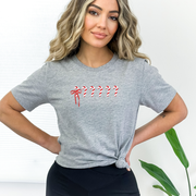 Woman wearing a grey holiday tee with a subtle 1 in 6 candy cane design honoring infertility awareness, standing in a festive outdoor setting.