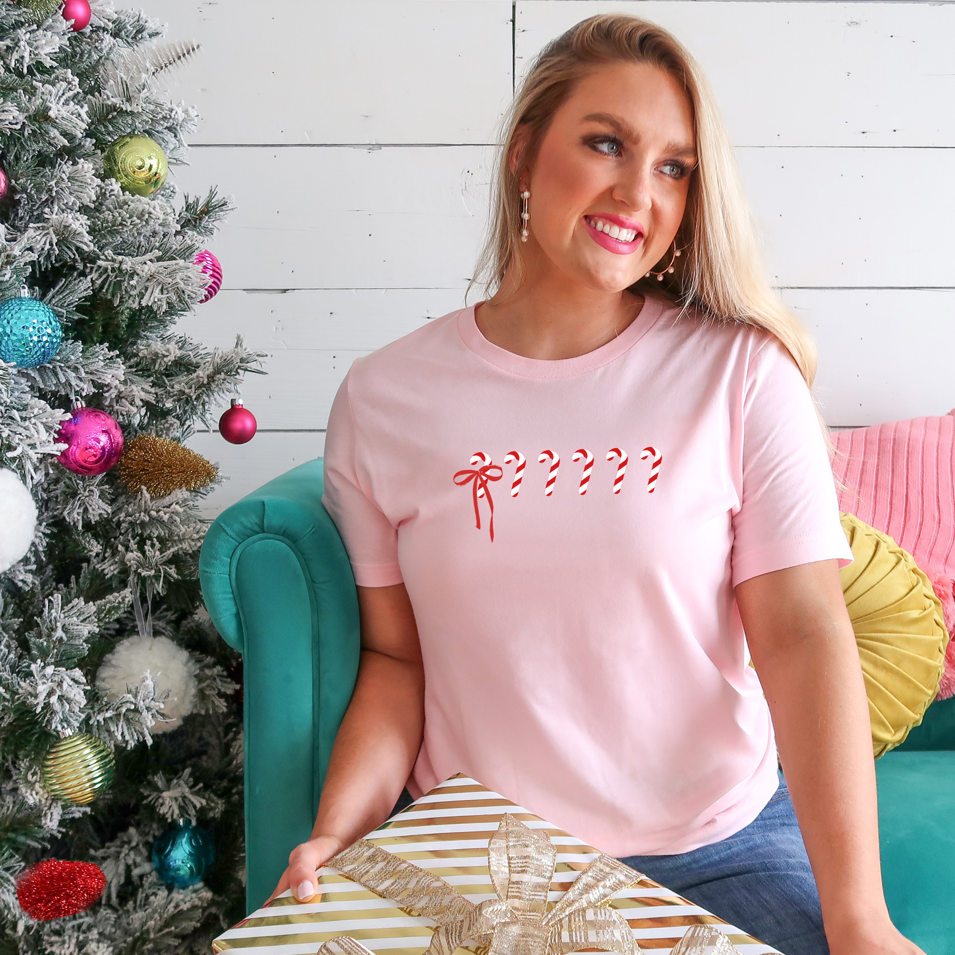 Woman wearing a pink holiday tshirt with a subtle 1 in 6 candy cane design honoring infertility awareness, standing in a festive indoor setting.
