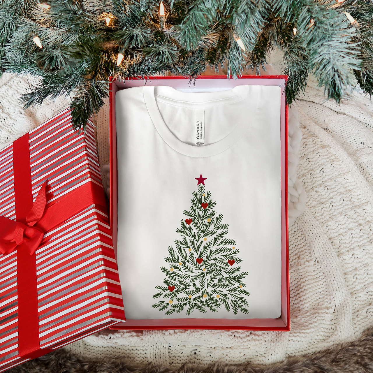 White t-shirt with Christmas tree design in a box under a decorated tree