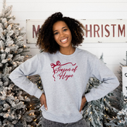 Woman wearing a gray sweatshirt with 'Season of Hope' text, standing in front of Christmas trees.