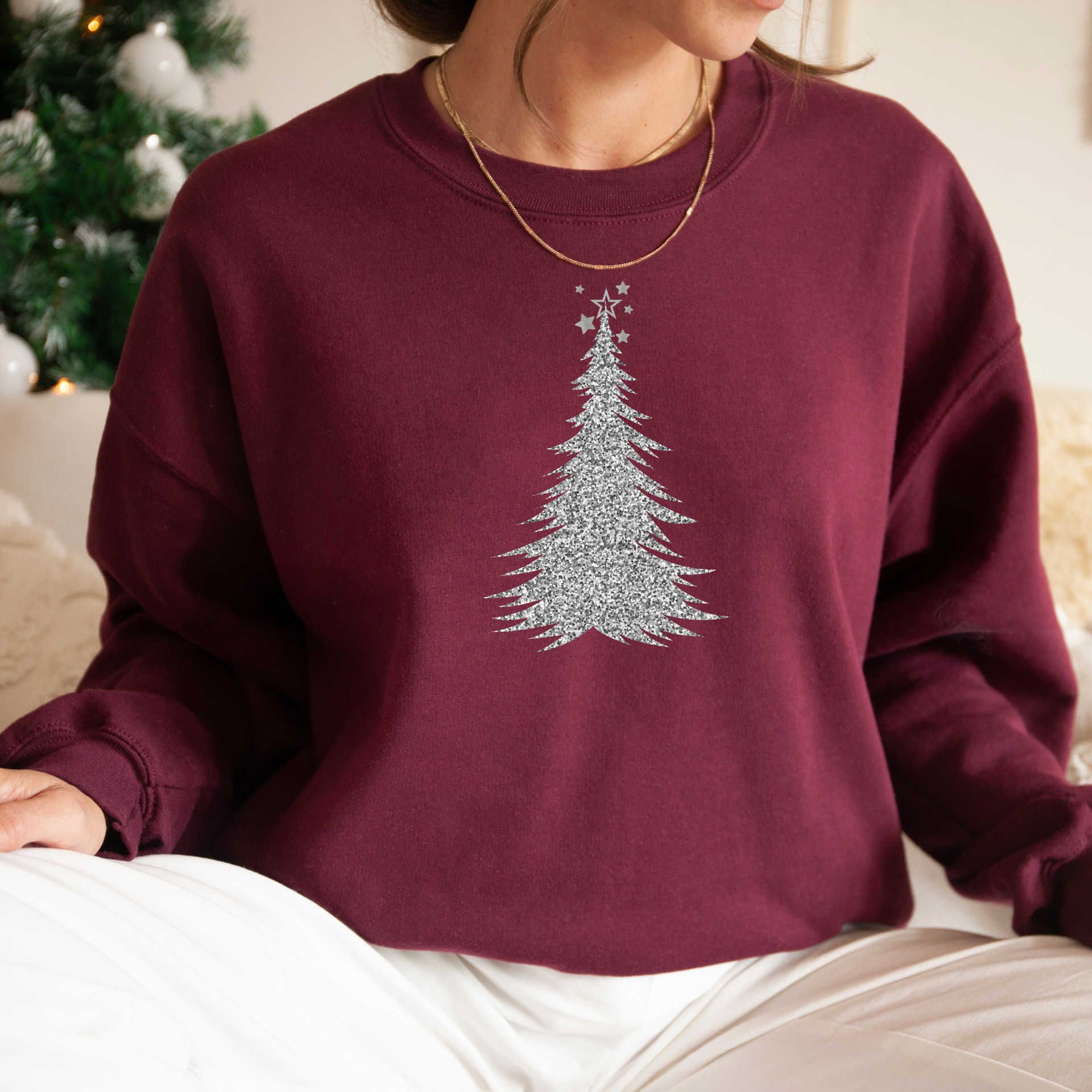 Person wearing a maroon sweatshirt with a Christmas tree design in front of a decorated Christmas tree.