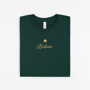 Green t-shirt with 'Believe' and a star in gold on a white background