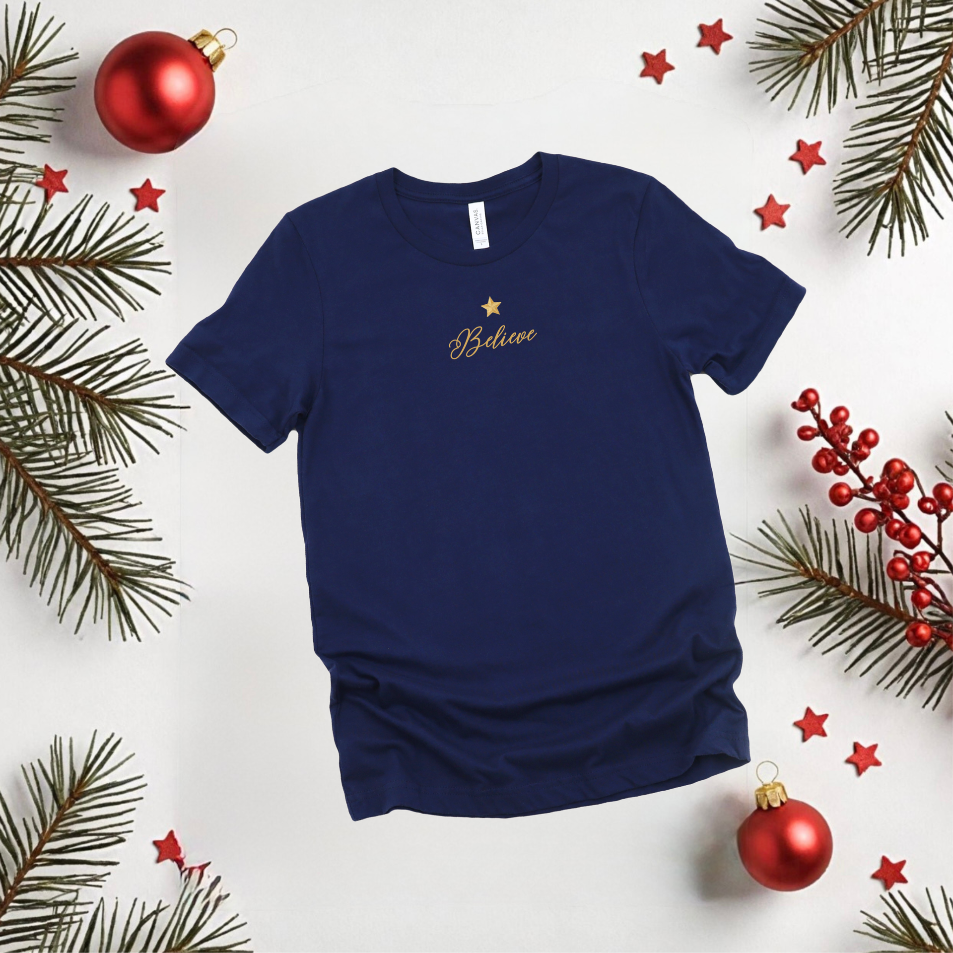 Navy blue t-shirt with 'Believe' text on a white background with Christmas decorations.